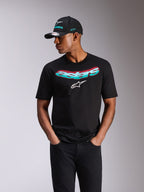 Alpinestars Ellipsoid CSF Tee, maglietta a maniche corte, nera, scritta Astars con sfumatura verde acqua e rosa e logo bianco, indossata da un modello con cappellino Alpinestars abbinato e jeans neri, streetwear casual motorsport