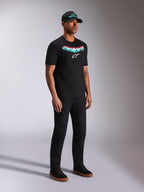 Alpinestars Ellipsoid CSF Tee, maglietta a maniche corte nera, grafica Astars con gradiente verde acqua e rosso e logo bianco, modello che indossa abbigliamento casual streetwear con cappellino e pantaloni neri