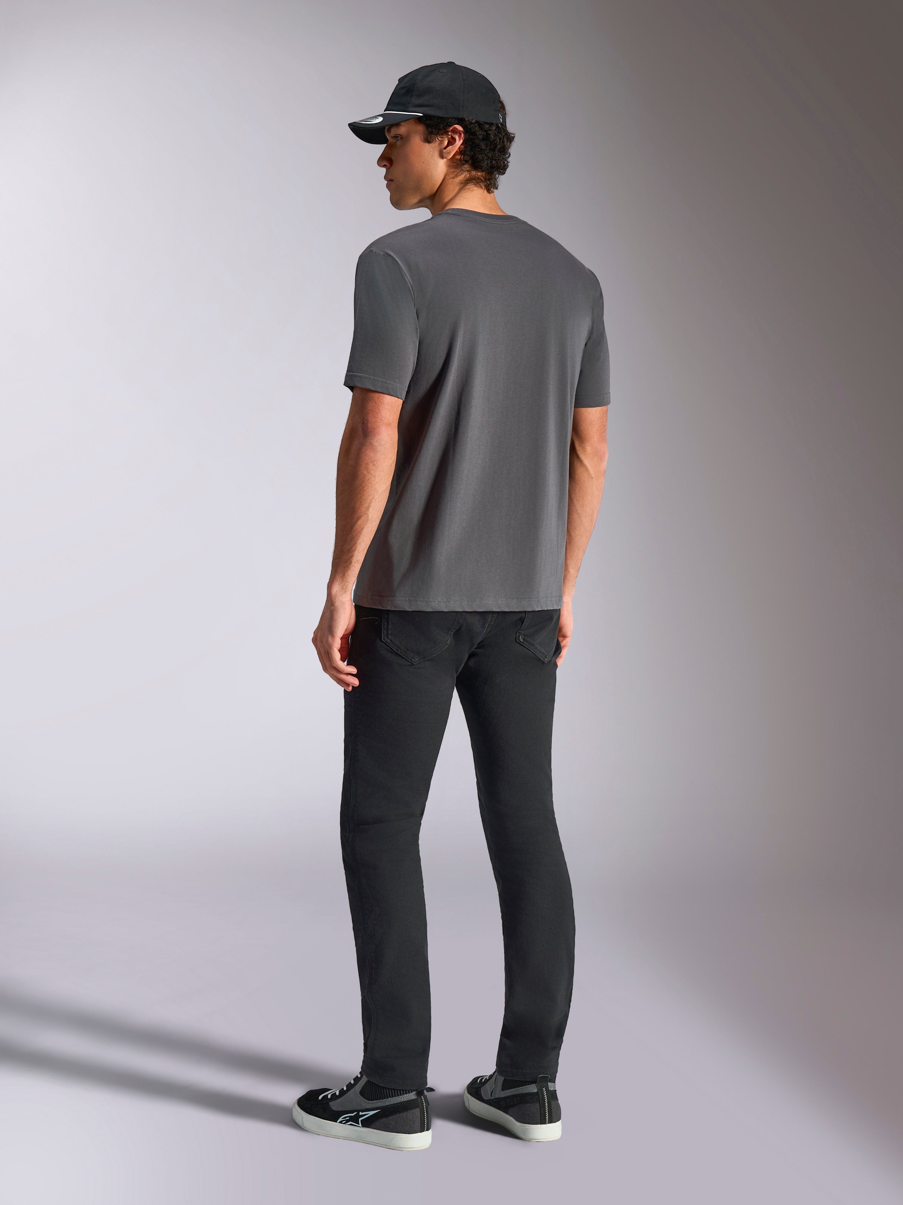 Alpinestars Ellipsoid CSF Tee, t-shirt a maniche corte, grigio antracite, vista posteriore, indossata da un modello con pantaloni neri e cappellino da baseball nero, abbigliamento casual motorsport streetwear