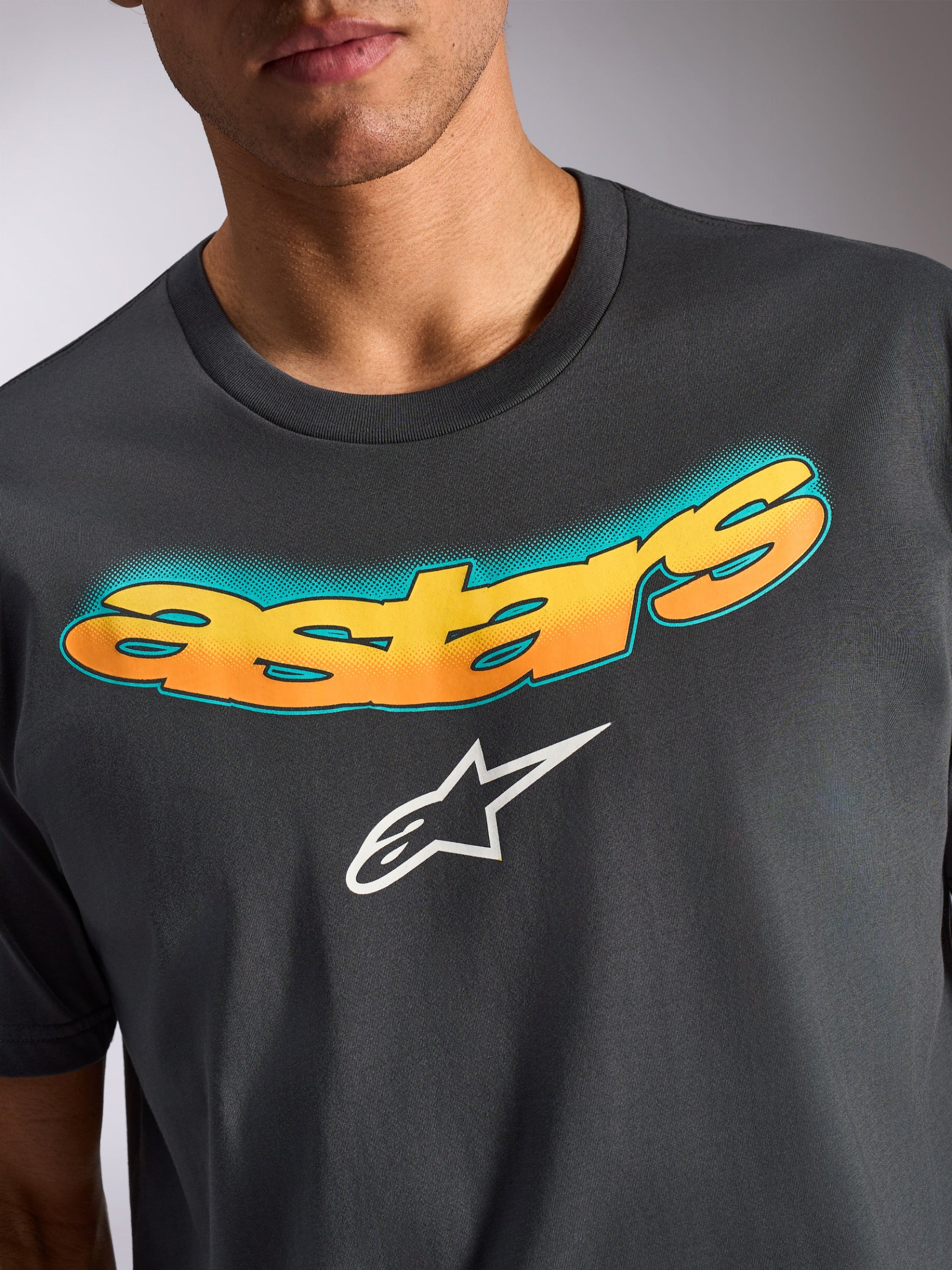 T-shirt Alpinestars Ellipsoid CSF, maglietta a maniche corte, grigio antracite, scritta 'astars' curva con gradiente giallo e arancione e motivo a puntini ottanio, logo a stella Alpinestars bianco, abbigliamento casual ispirato al motorsport