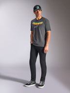 Alpinestars Ellipsoid CSF Tee, t-shirt a maniche corte, grigio antracite, con scritta Astars curva con gradiente di colore e logo bianco, indossata da un modello con pantaloni neri e cappellino, streetwear casual motorsport