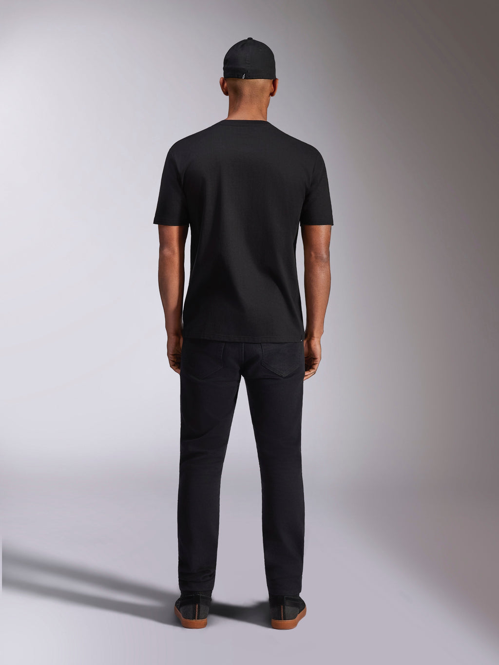 Alpinestars Plate CSF Tee, t-shirt a maniche corte, nera, vista posteriore su modello, indossata con cappellino e pantaloni neri, streetwear casual da motorsport