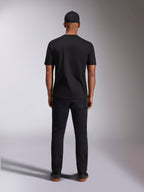 Alpinestars Plate CSF Tee, t-shirt a maniche corte, nera, vista posteriore su modello, indossata con cappellino e pantaloni neri, streetwear casual da motorsport