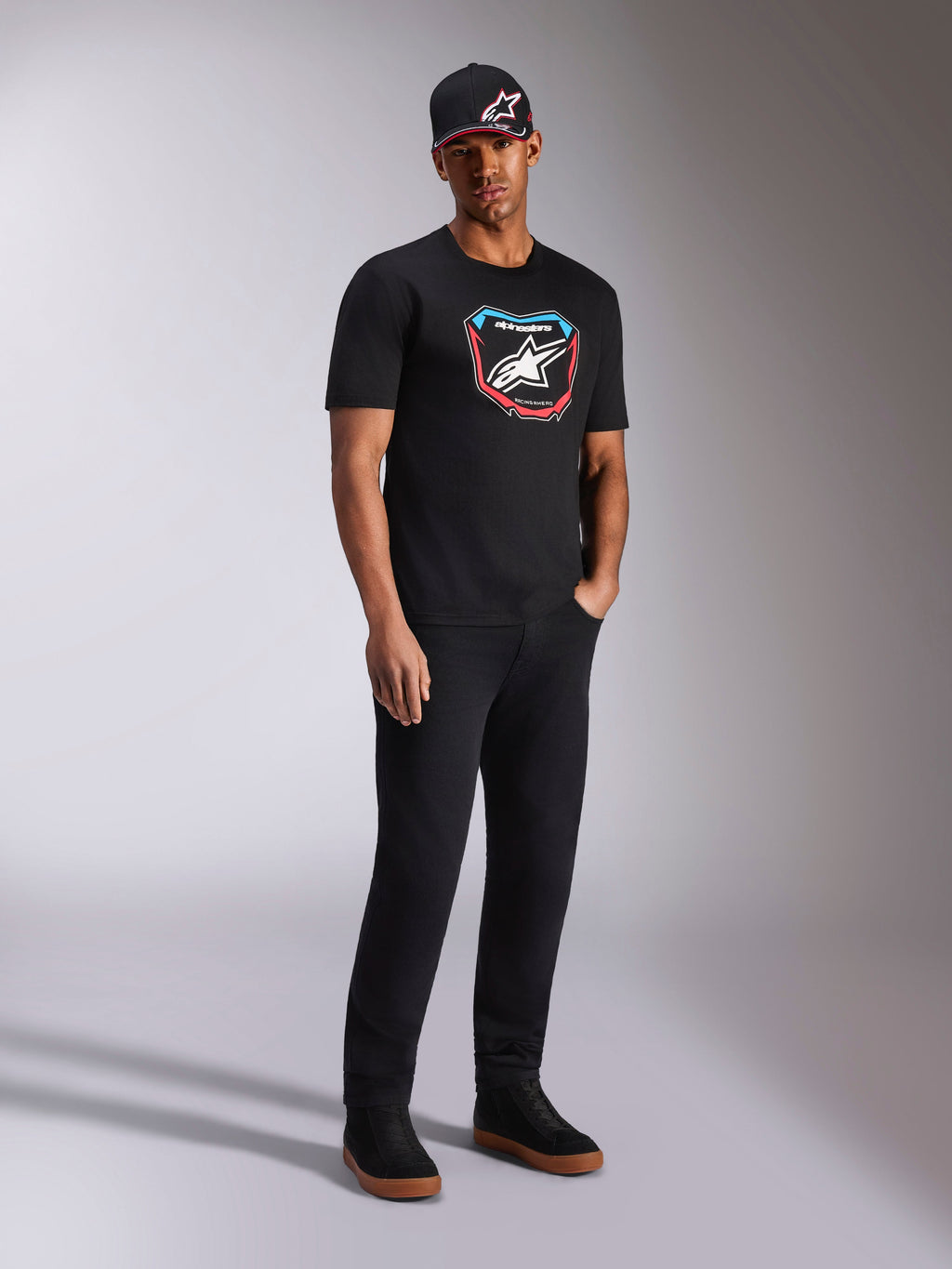 Alpinestars Plate CSF Tee, t-shirt a maniche corte, nero, grafica frontale colorata stile tabella MX con logo a stella, indossata da un modello con cappellino e pantaloni neri, streetwear casual ispirato al motorsport