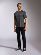 Alpinestars Pop Helmet CSF Tee, t-shirt a maniche corte, grigio antracite, con logo Alpinestars rosa sul petto, indossata da un modello uomo con pantaloni neri e sneaker, abbigliamento streetwear casual motorsport