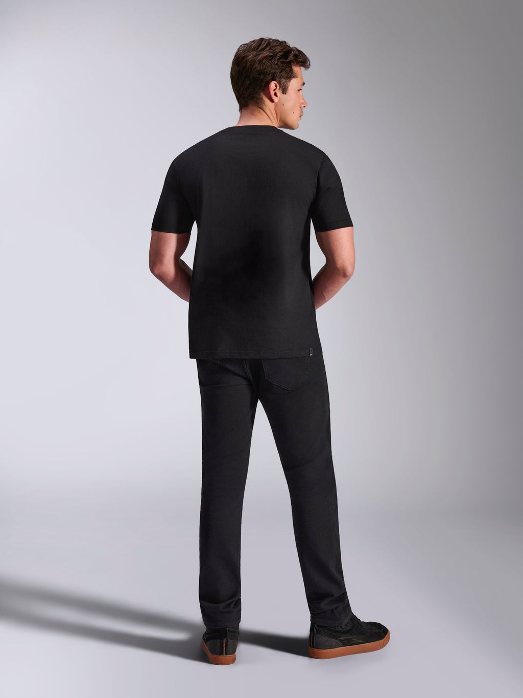 Alpinestars Abus CSF Tee, T-shirt a maniche corte, nero, vista posteriore su modello abbinata a pantaloni neri, abbigliamento sportivo casual da motorsport