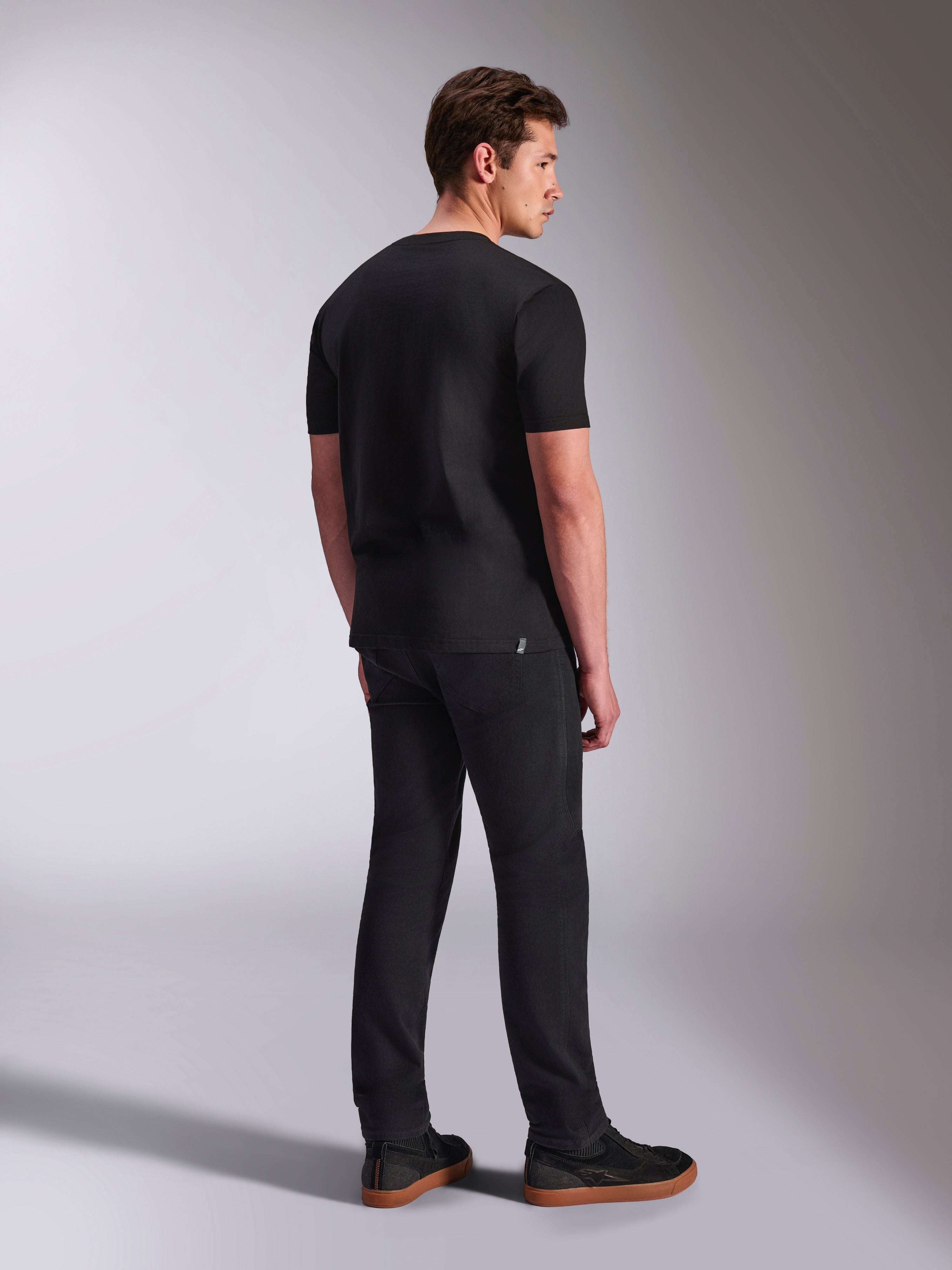 Alpinestars Abus CSF Tee, t-shirt a maniche corte, nero, vista posteriore su modello maschile, streetwear casual ispirato al motorsport, abbinata a pantaloni scuri e sneakers