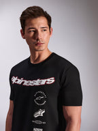 Alpinestars Abus CSF Tee, T-shirt a maniche corte, nera, indossata da un modello, con logo Alpinestars bianco con bordo rosso e loghi grafici multipli impilati sul petto, streetwear casual motorsport