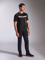 T-shirt Alpinestars Abus CSF, maglietta a maniche corte, nera, con logo Alpinestars curvo rosso e bianco e grafiche verticali impilate, indossata con pantaloni neri e sneaker, streetwear casual ispirato al motorsport