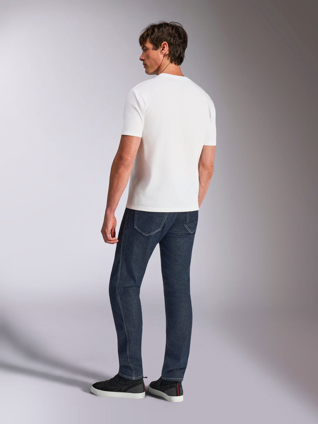 Alpinestars Abus CSF Tee, T-shirt a maniche corte, bianca, vista posteriore su modello che indossa jeans blu scuro e sneakers nere, design casual ispirato al motorsport
