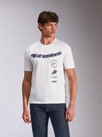 Alpinestars Abus CSF Tee, t-shirt a maniche corte, bianca, logo Alpinestars curvo con grafiche multiple sovrapposte sul petto, indossata da un modello con jeans in denim scuro, abbigliamento streetwear casual ispirato al motorsport