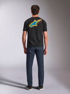 Alpinestars Angler CSF Tee, t-shirt a maniche corte, nero, vista posteriore del modello con grande logo Astars a stella multicolore e scritta 'RACING AHEAD', abbinata a jeans blu scuro, streetwear casual motorsport