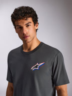 Alpinestars Angler CSF Tee, t-shirt a maniche corte, grigio antracite, indossata da un modello, con logo Astars multicolore sul petto, streetwear casual ispirato al motorsport