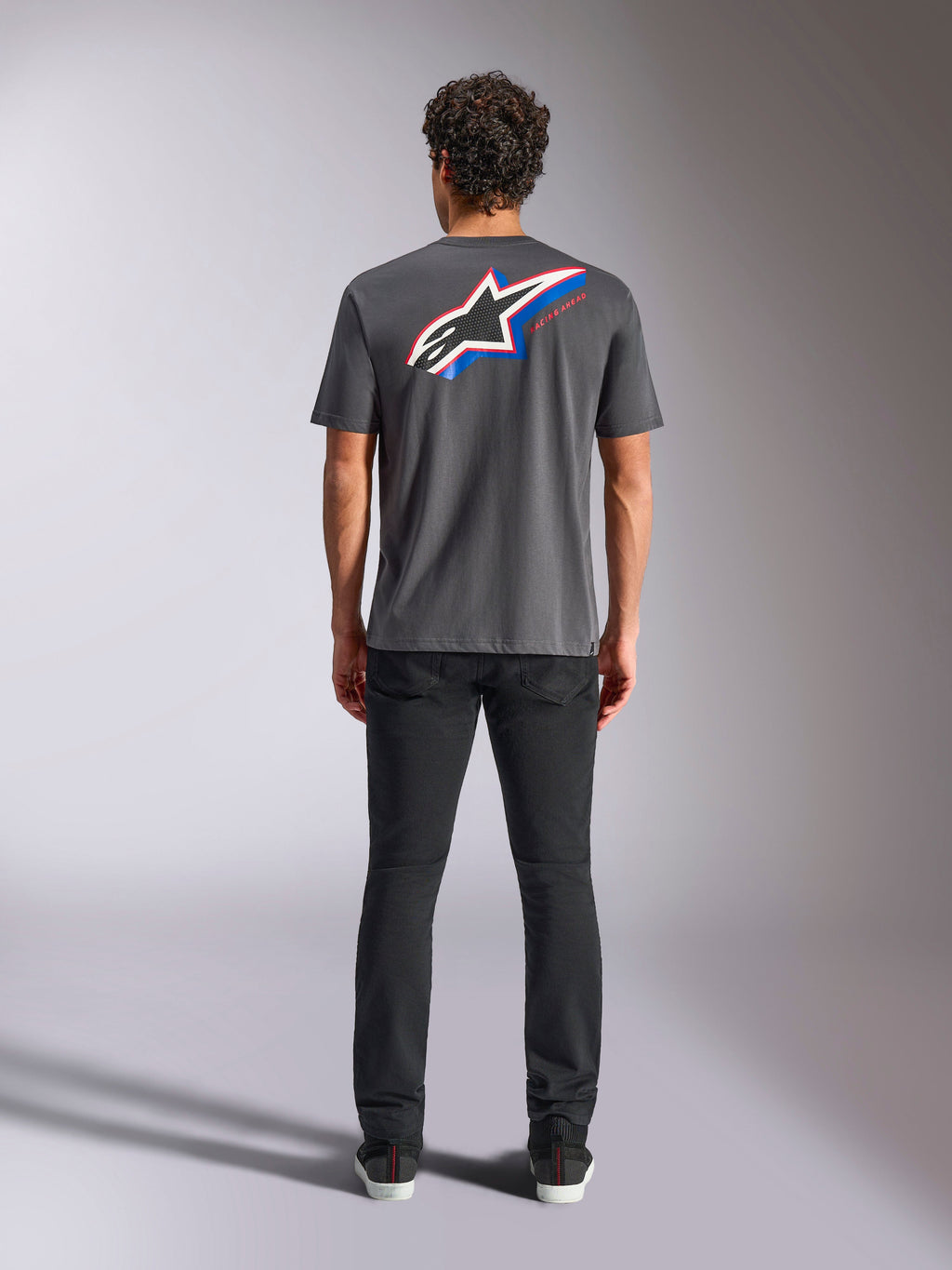 Alpinestars Angler CSF Tee, maglietta a maniche corte, carbone, grande logo Astars multicolore sul retro con accenti rossi e blu, vista posteriore su modello, streetwear casual ispirato al motorsport