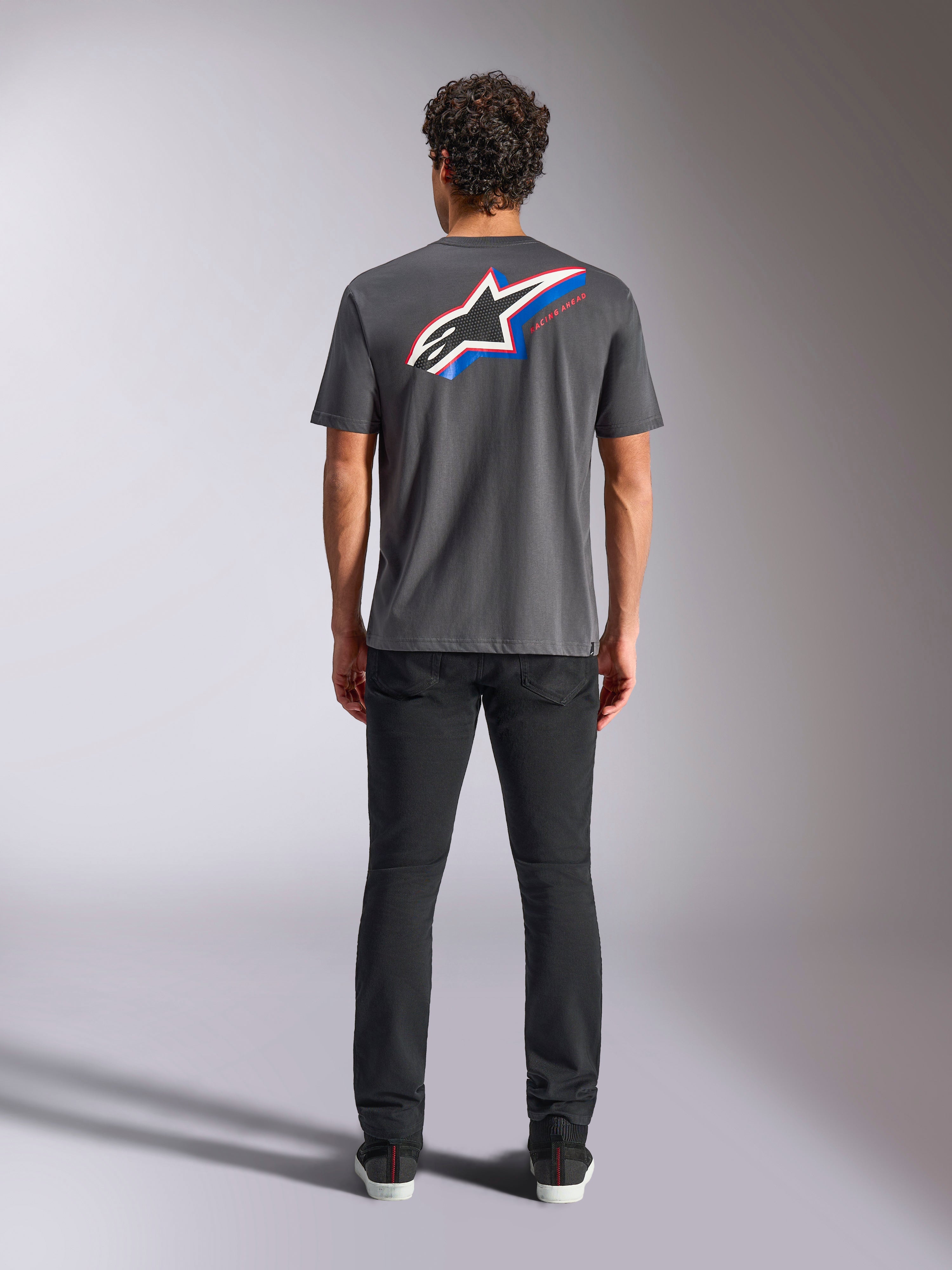 Alpinestars Angler CSF Tee, maglietta a maniche corte, carbone, grande logo Astars multicolore sul retro con accenti rossi e blu, vista posteriore su modello, streetwear casual ispirato al motorsport