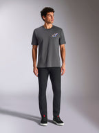 Alpinestars Angler CSF Tee, maglietta a maniche corte, antracite, con vivace logo Astars multicolore sul petto, indossata da un modello con pantaloni neri e sneakers, streetwear casual motorsport