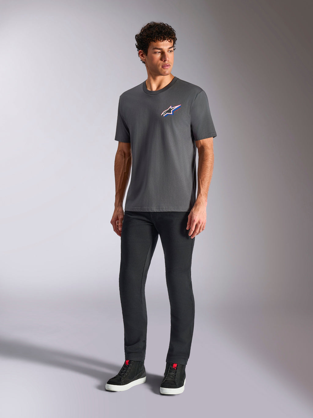 Alpinestars Angler CSF Tee, maglietta a maniche corte, grigio antracite, logo Astars multicolore sul petto, indossata con pantaloni neri e sneakers, streetwear casual motorsport