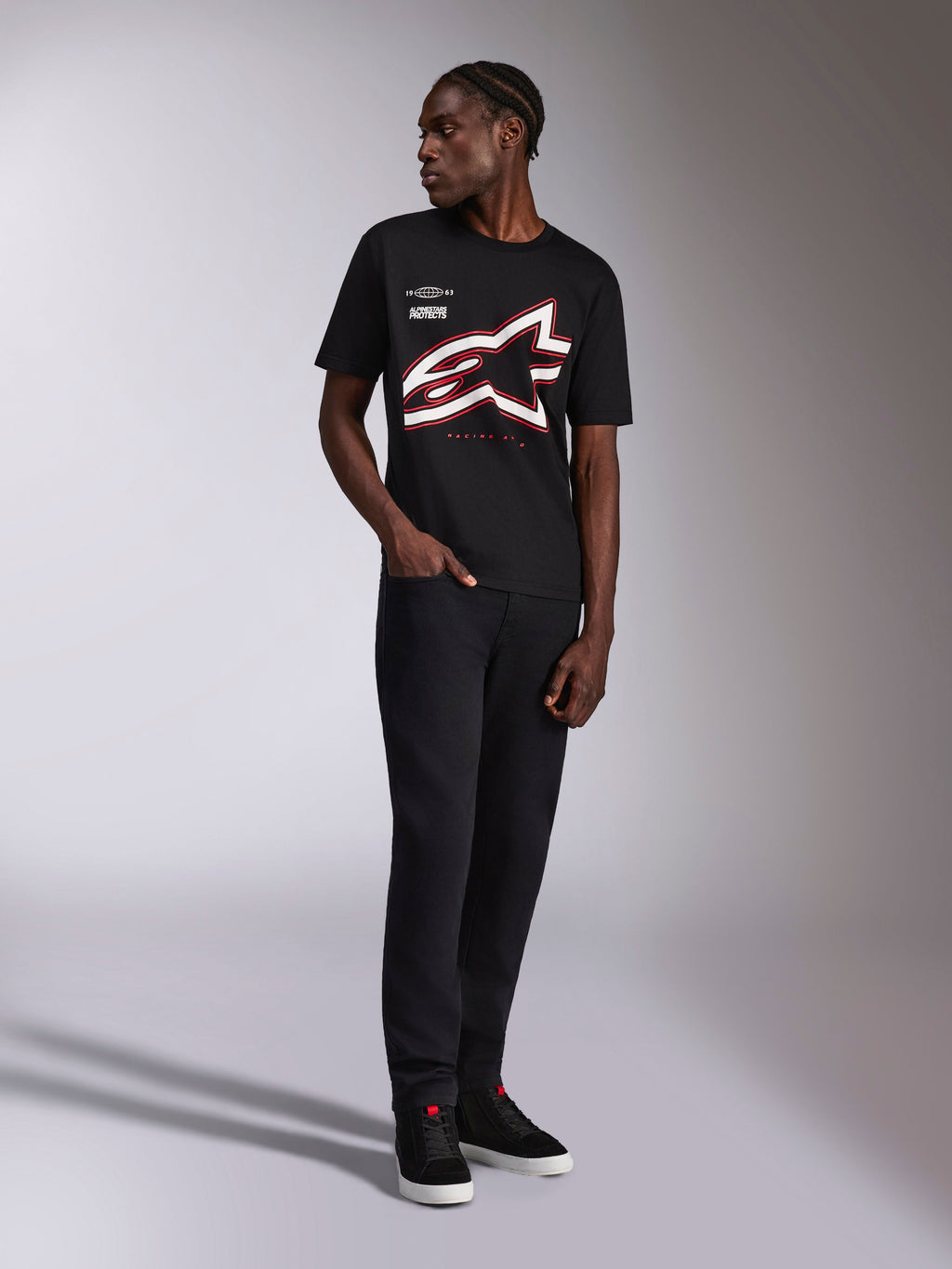 Alpinestars Authority CSF Tee, t-shirt a maniche corte, nero, grande logo Astars profilato rosso e bianco ritagliato, indossata da un modello con pantaloni e sneakers neri, streetwear motorsport casual