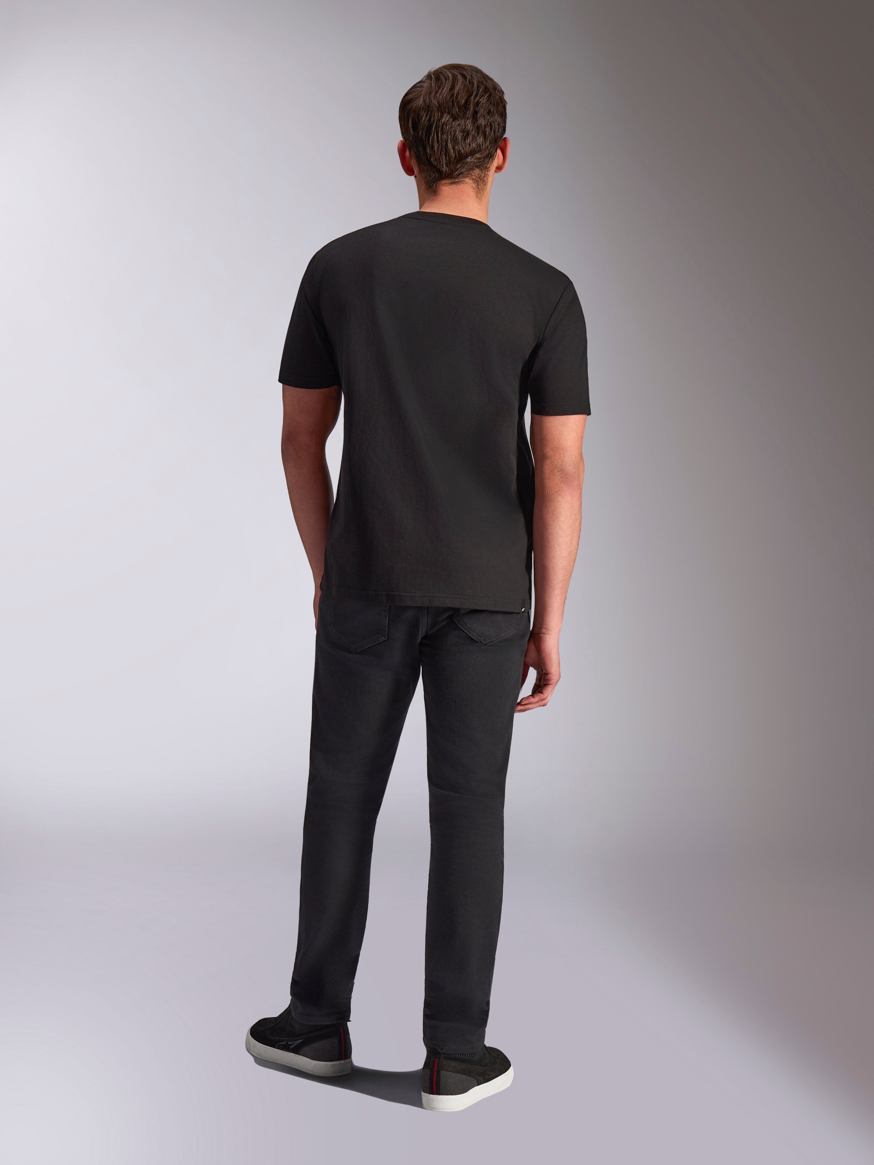 Alpinestars Trifecta CSF Tee, t-shirt a maniche corte, nero, vista posteriore su modello, indossata con pantaloni neri e sneakers nere, streetwear casual ispirato al motorsport