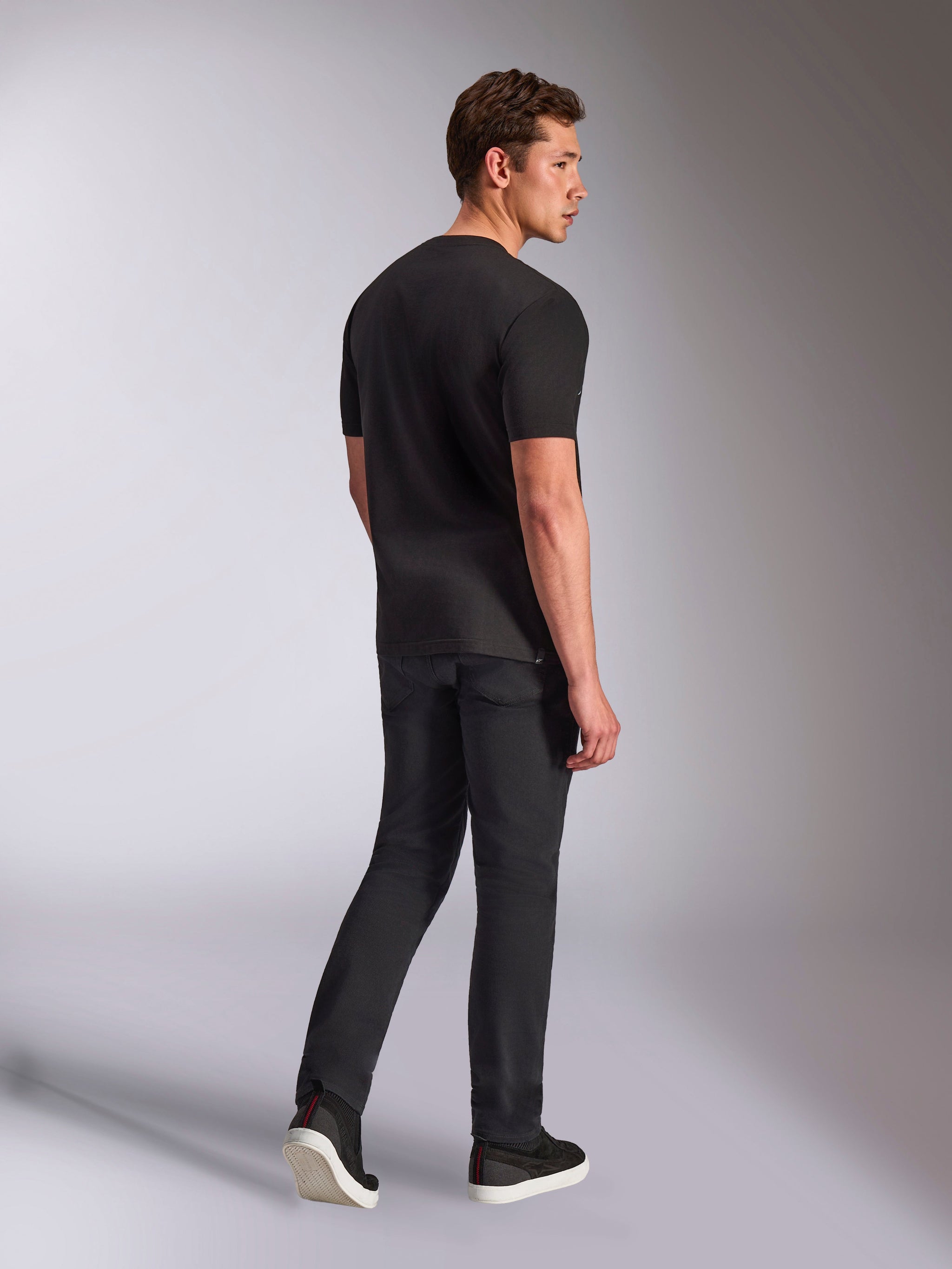 Alpinestars Trifecta CSF Tee, t-shirt a maniche corte, nero, vista posteriore di un uomo che indossa la maglietta con jeans neri e sneakers, abbigliamento casual motorsport streetwear