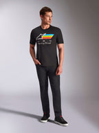 Alpinestars Trifecta CSF Tee, t-shirt a maniche corte, nero, con logo Astars bianco con strisce ciano, gialle e arancioni e scritta 'Racing Ahead', indossata da un modello con pantaloni neri e sneakers per un look motorsport streetwear casual