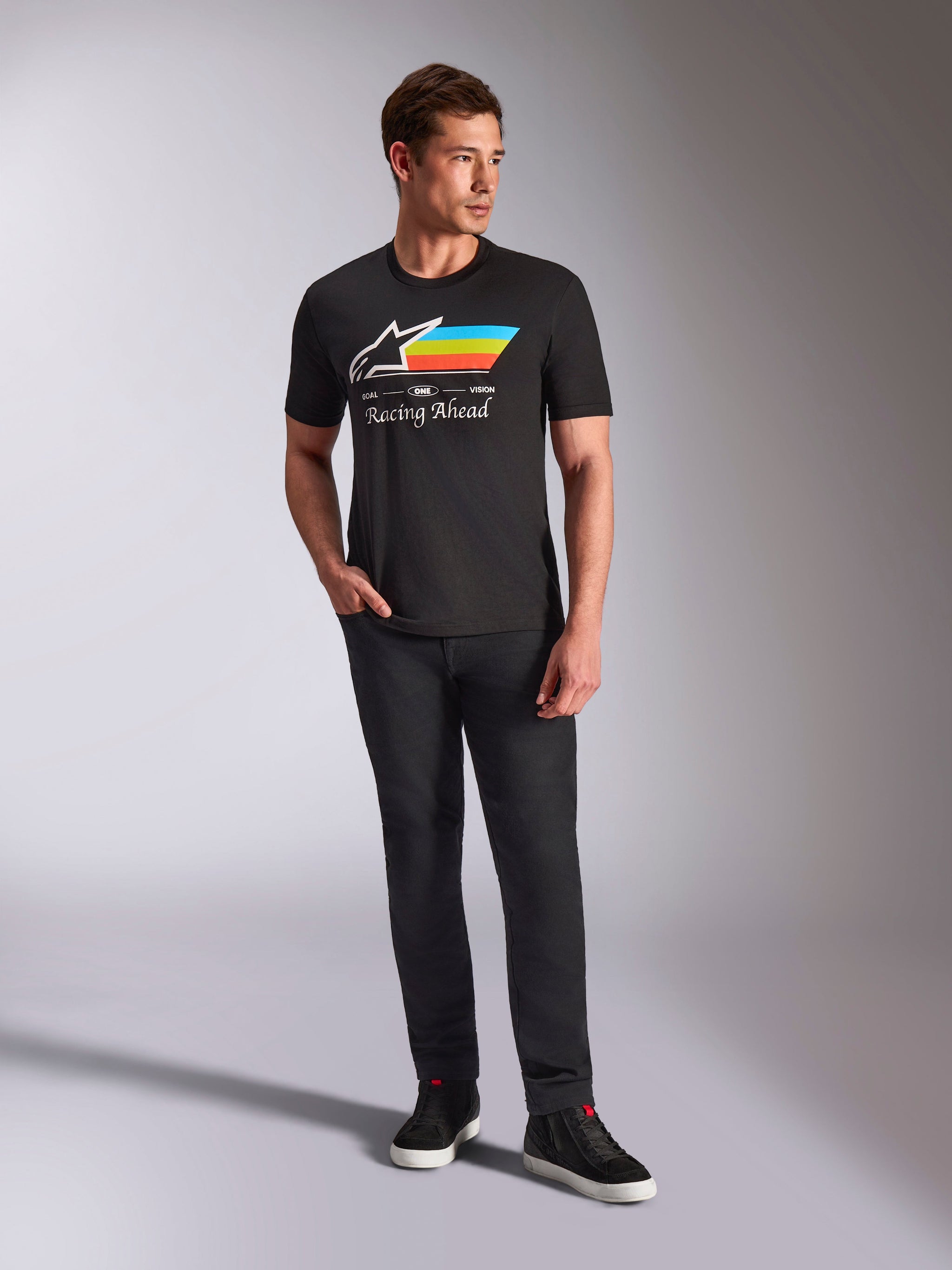 Alpinestars Trifecta CSF Tee, t-shirt a maniche corte, nero, con logo Astars bianco con strisce ciano, gialle e arancioni e scritta 'Racing Ahead', indossata da un modello con pantaloni neri e sneakers per un look motorsport streetwear casual