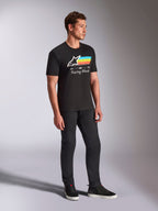 Alpinestars Trifecta CSF Tee, maglietta a maniche corte nera, logo Astars bianco con strisce blu, gialle e arancioni e grafica 'Racing Ahead', indossata da un modello con pantaloni neri e sneakers, abbigliamento lifestyle casual ispirato al motorsport