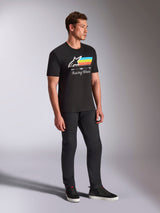 Alpinestars Trifecta CSF Tee, maglietta a maniche corte nera, logo Astars bianco con strisce blu, gialle e arancioni e grafica 'Racing Ahead', indossata da un modello con pantaloni neri e sneakers, abbigliamento lifestyle casual ispirato al motorsport