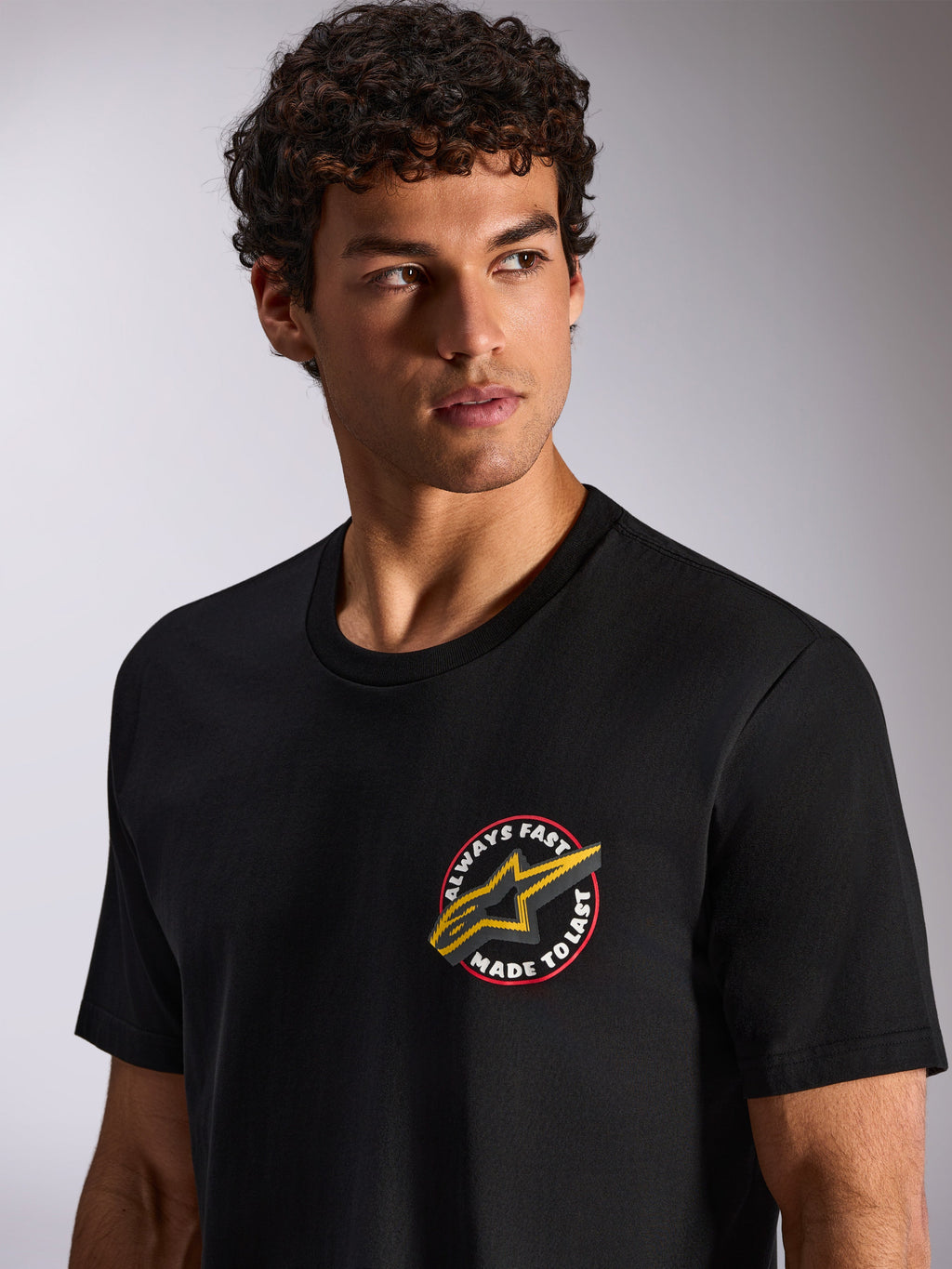 Alpinestars Aorbit CSF Tee, t-shirt a maniche corte, nero, grafica circolare sul petto Always Fast Made to Last con logo Astars giallo, indossata da un modello, streetwear casual motorsport