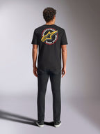 T-shirt Alpinestars Aorbit CSF, maglietta a maniche corte, nero, indossata da un modello vista dal retro con pantaloni neri, con grande grafica 'Always Fast Made to Last' e logo Astars giallo, streetwear casual a tema motorsport