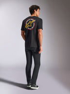 Alpinestars Aorbit CSF Tee, t-shirt a maniche corte, nero, vista posteriore con grande logo Astars giallo e grafica circolare 'Always Fast Made to Last', indossata con jeans neri e sneakers casual, stile streetwear ispirato al motorsport