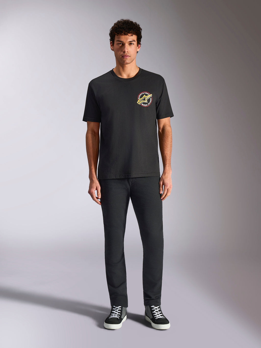 Alpinestars Aorbit CSF Tee, t-shirt a maniche corte, nera, logo circolare con scritta 'Always Fast Made to Last' sul petto, indossata da un modello con pantaloni neri e sneakers, streetwear casual ispirato al motorsport