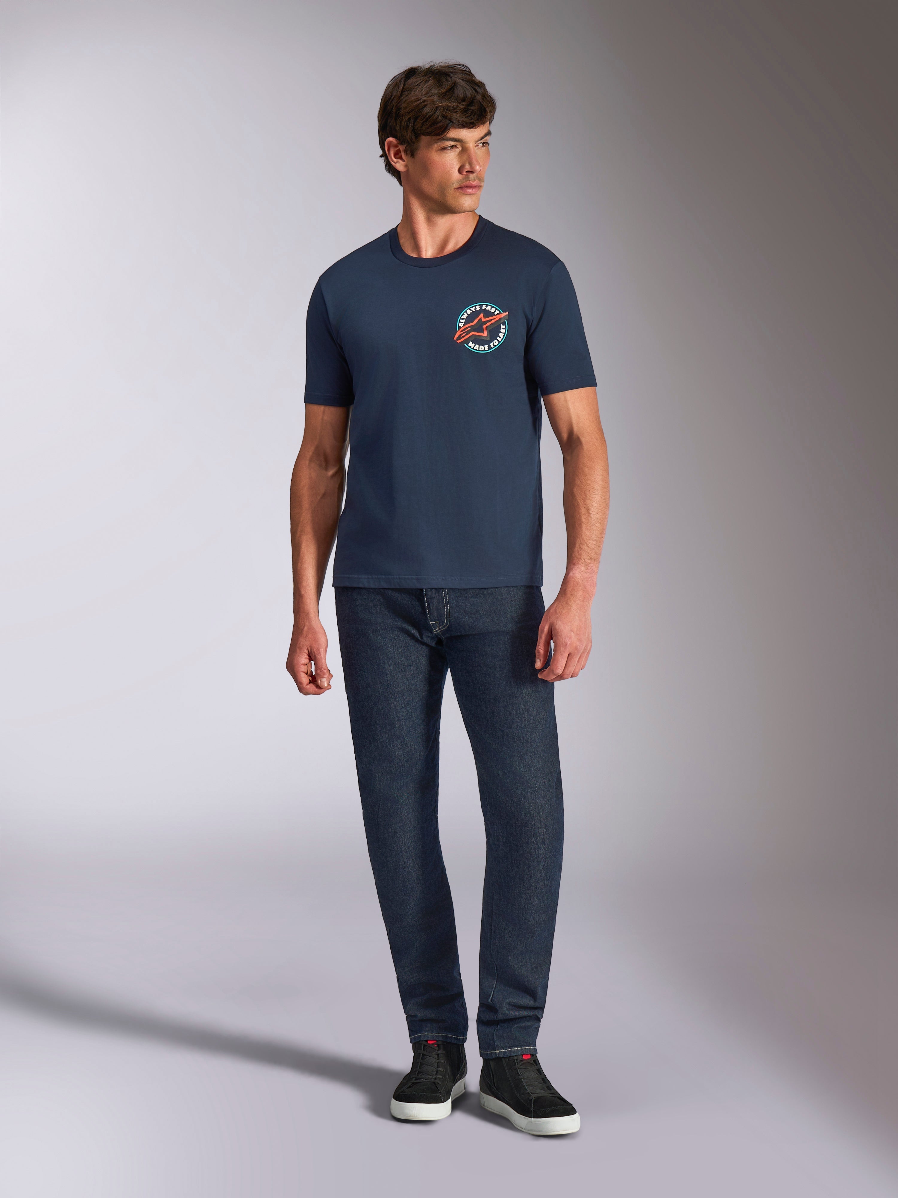 Alpinestars Aorbit CSF Tee, t-shirt a maniche corte, blu navy, grafica circolare sul petto con testo Always Fast Made to Last, indossata con jeans scuri e sneakers, abbigliamento casual motorsport lifestyle