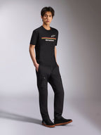 Alpinestars Lanes CSF Tee, t-shirt a maniche corte, nera, loghi Astars e Alpinestars a strisce multicolore sul petto, indossata da un modello con pantaloni cargo neri, streetwear casual motorsport