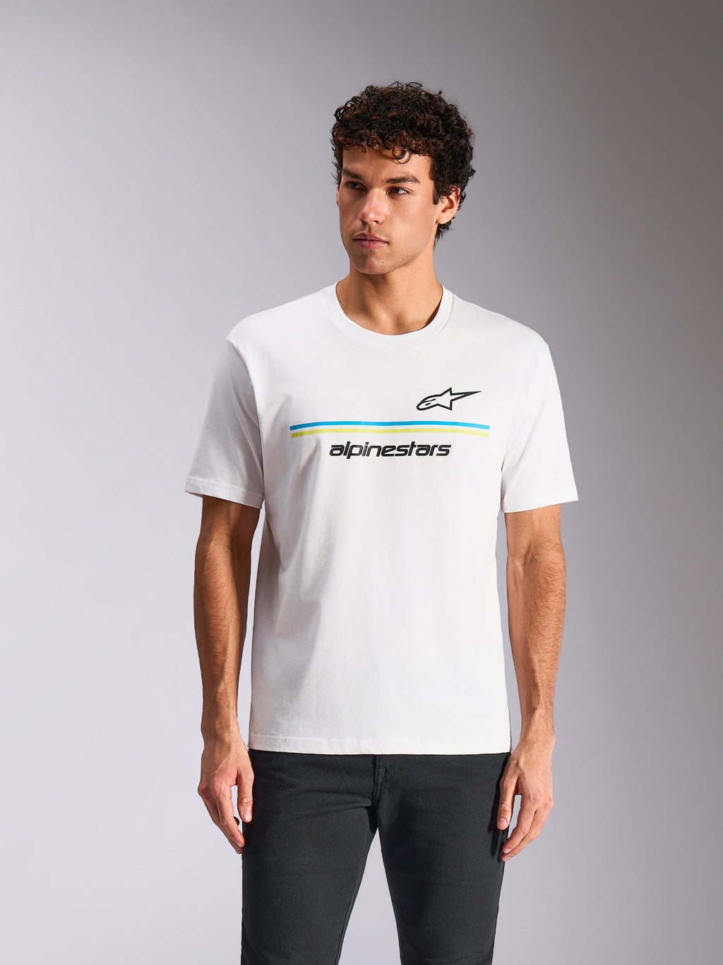 Alpinestars Lanes CSF Tee, t-shirt a maniche corte, bianca, con logo Astars nero sopra strisce orizzontali blu e verde lime e scritta 'alpinestars', indossata da un modello, streetwear casual motorsport