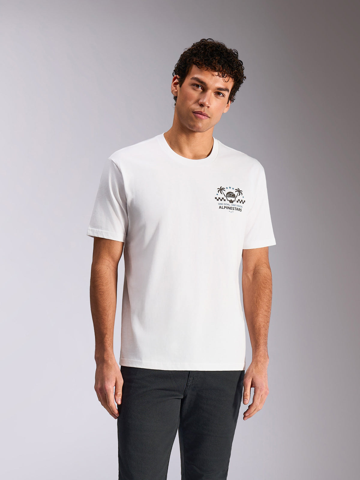Alpinestars Order CSF Tee, t-shirt a maniche corte, bianca, grafica sul petto con casco e palme, indossata da un modello con pantaloni scuri, streetwear casual ispirato al motorsport