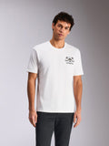 Alpinestars Order CSF Tee, t-shirt a maniche corte, bianca, grafica sul petto con casco e palme, indossata da un modello con pantaloni scuri, streetwear casual ispirato al motorsport