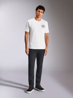 Alpinestars Order CSF Tee, t-shirt a maniche corte, bianco, piccola grafica nera sul petto con casco e palme, streetwear casual da motorsport, indossata da un modello con pantaloni neri e sneakers