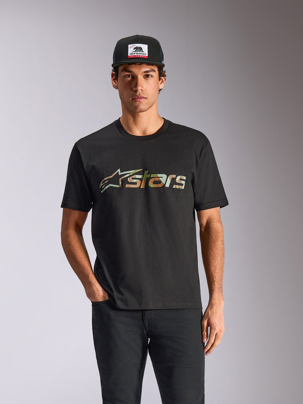 Maglietta Alpinestars Verdure Camo CSF, t-shirt a maniche corte, nero, indossata da un modello con cappellino e pantaloni neri, con logo Astars frontale con stampa camo, streetwear casual motorsport