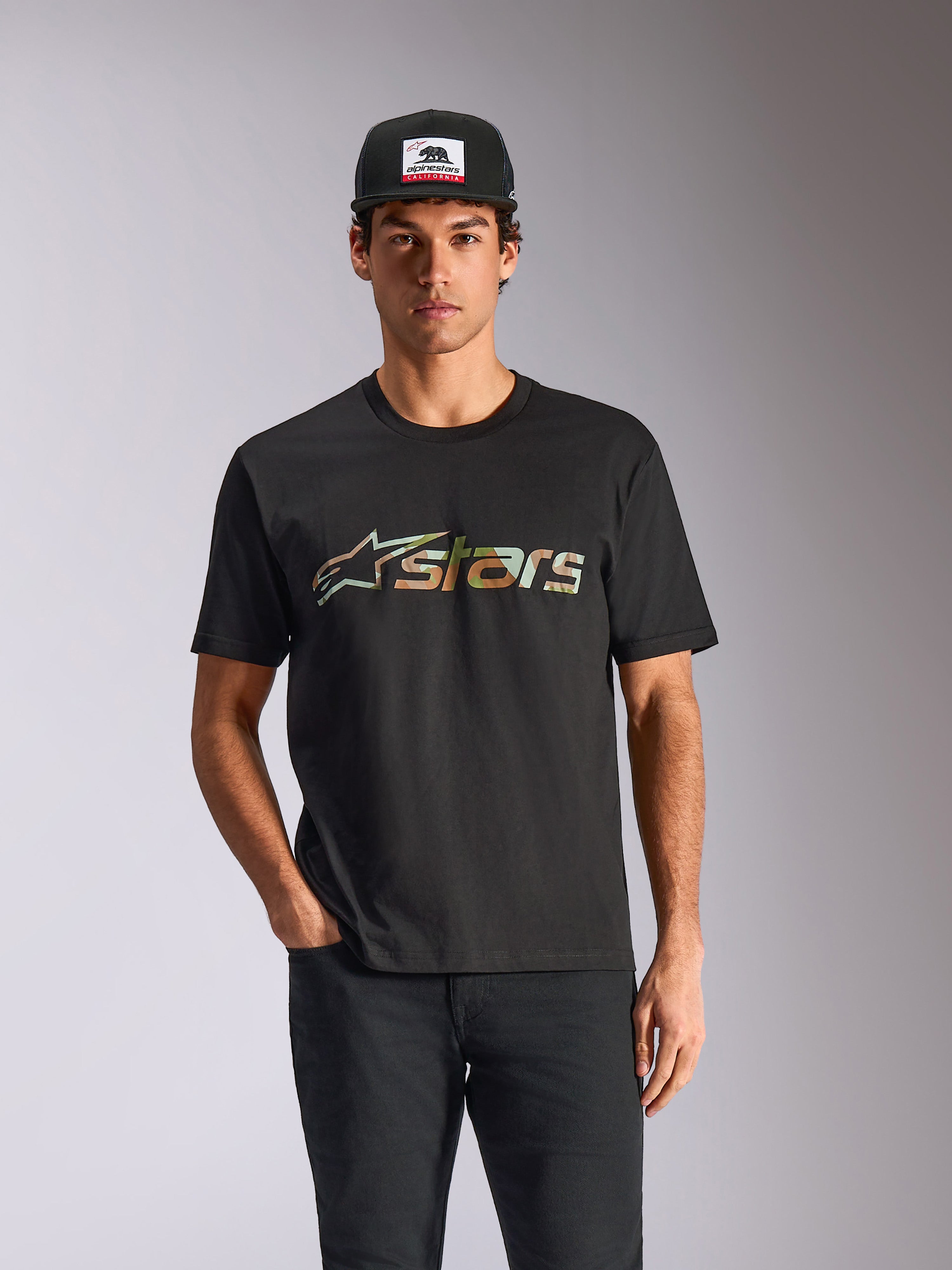 Maglietta Alpinestars Verdure Camo CSF, t-shirt a maniche corte, nero, indossata da un modello con cappellino e pantaloni neri, con logo Astars frontale con stampa camo, streetwear casual motorsport