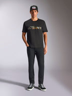 Alpinestars Verdure Camo CSF Tee, t-shirt a maniche corte, nera, con logo Astars a motivo camouflage sul petto, indossata da un modello con cappellino nero e pantaloni neri, streetwear casual motorsport