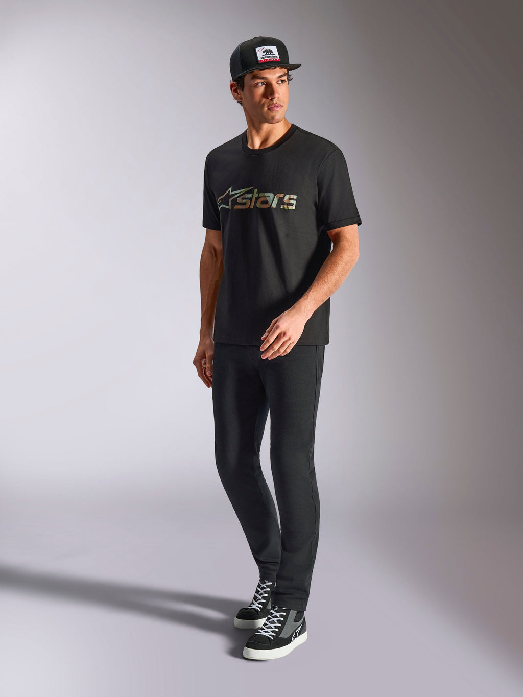 Alpinestars Verdure Camo CSF Tee, t-shirt a maniche corte, nero, con logo Astars con riempimento camo sul petto, indossata da un modello con cappellino e pantaloni neri, streetwear casual motorsport