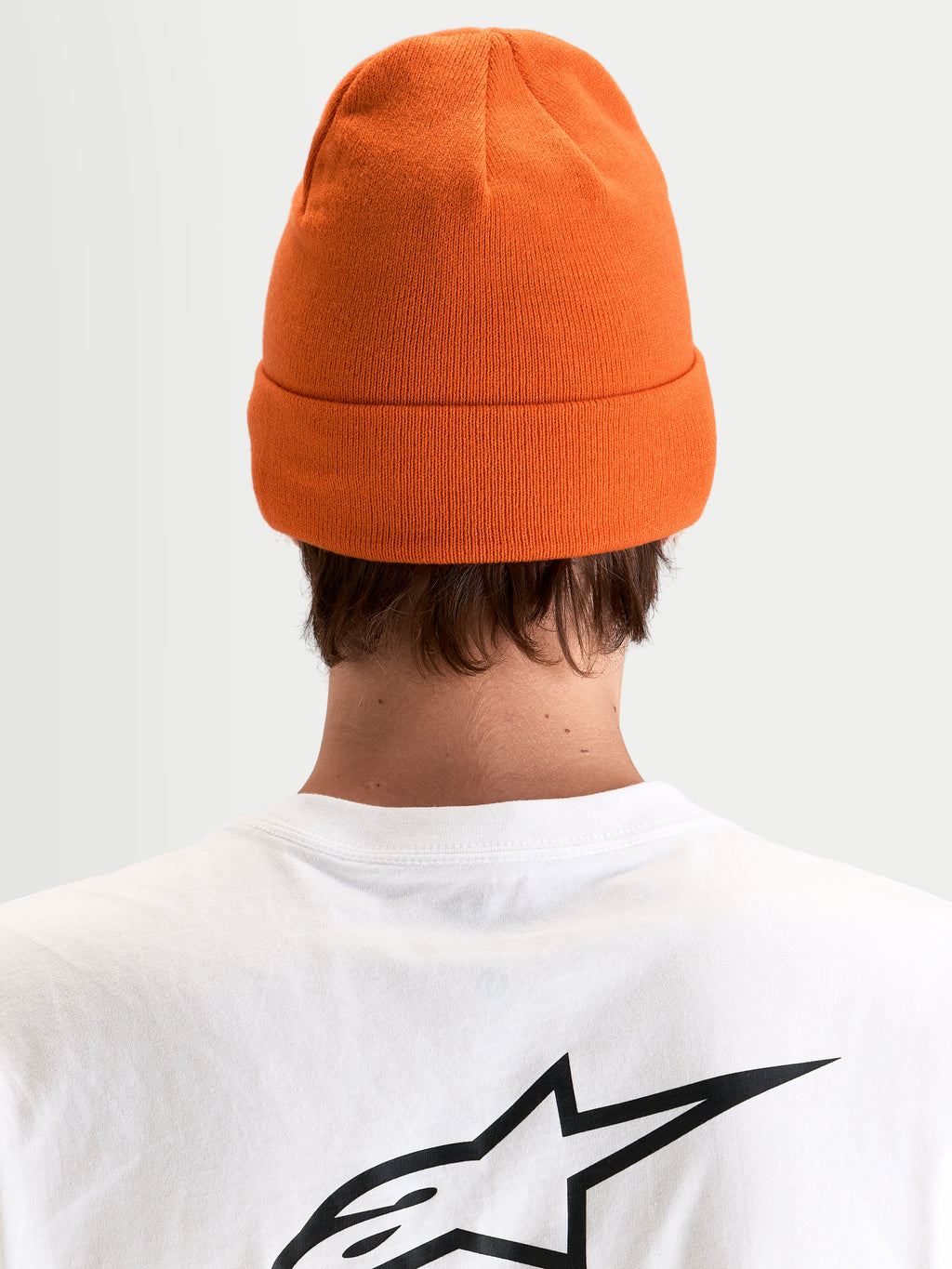 Alpinestars Berretto Augment Cuff, berretto in maglia arancione con design risvoltato e silhouette a vestibilità profonda, vista posteriore di un modello che indossa una maglietta bianca con logo Astar nero