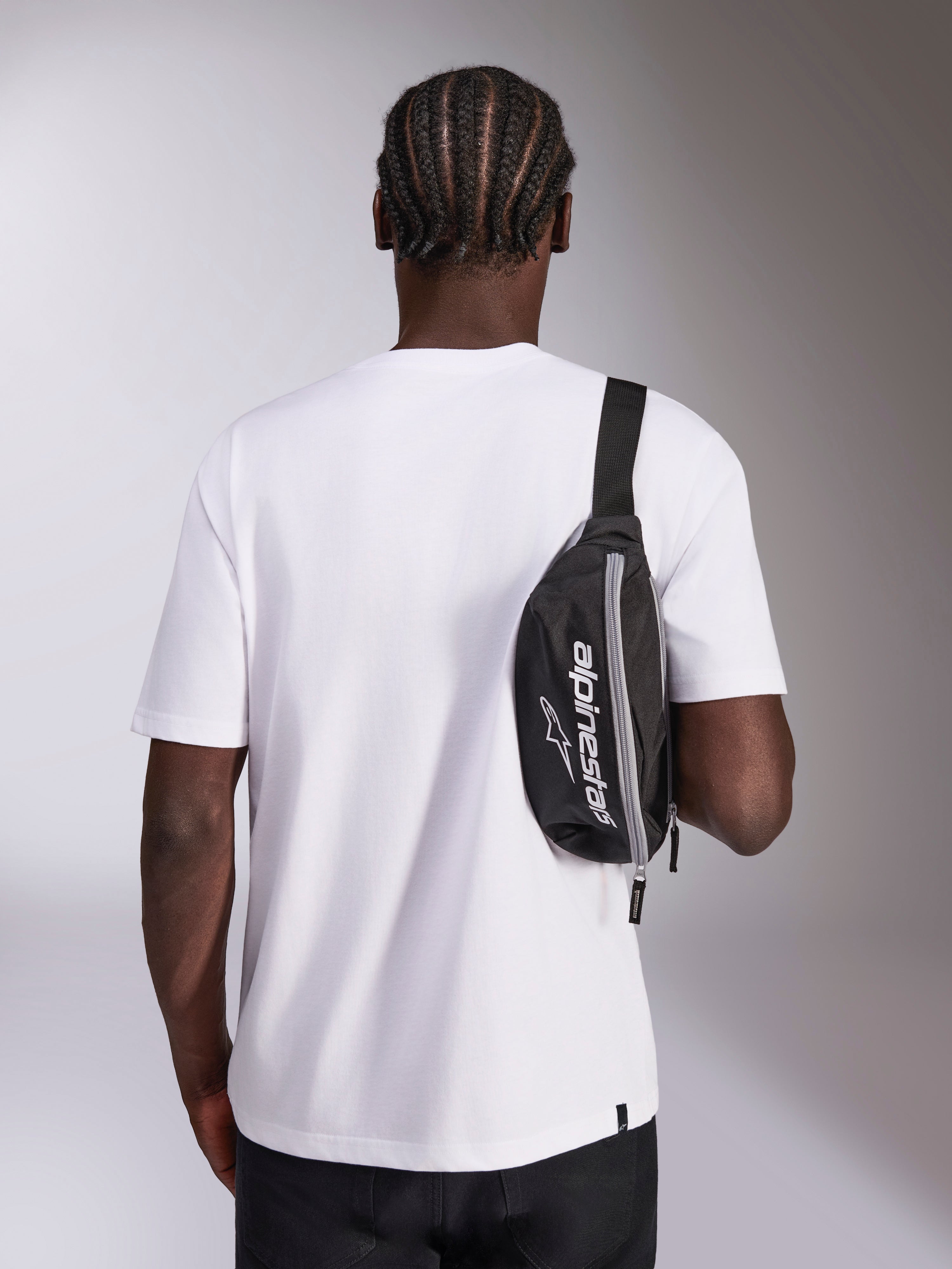 Marsupio Alpinestars Only Linear, nero con logo Alpinestars bianco, indossato a tracolla sopra una t-shirt bianca, accessorio streetwear casual ispirato al motorsport