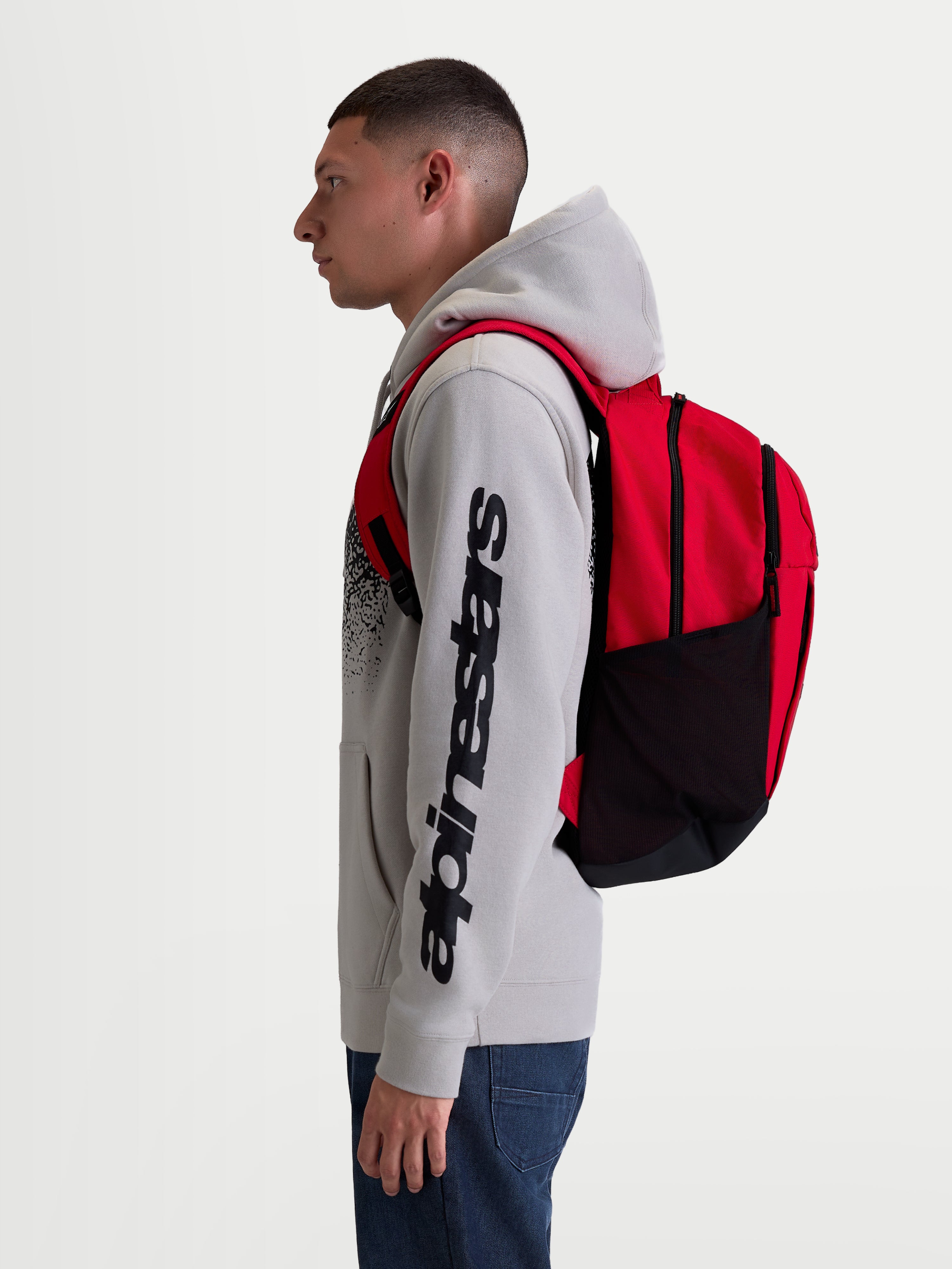 Alpinestars zaino GFX Boss, zaino sportivo da 20L per uomo e donna, rosso e nero, in poliestere resistente con tasche laterali in rete e spallacci imbottiti, vista laterale su modello per uso quotidiano e urbano