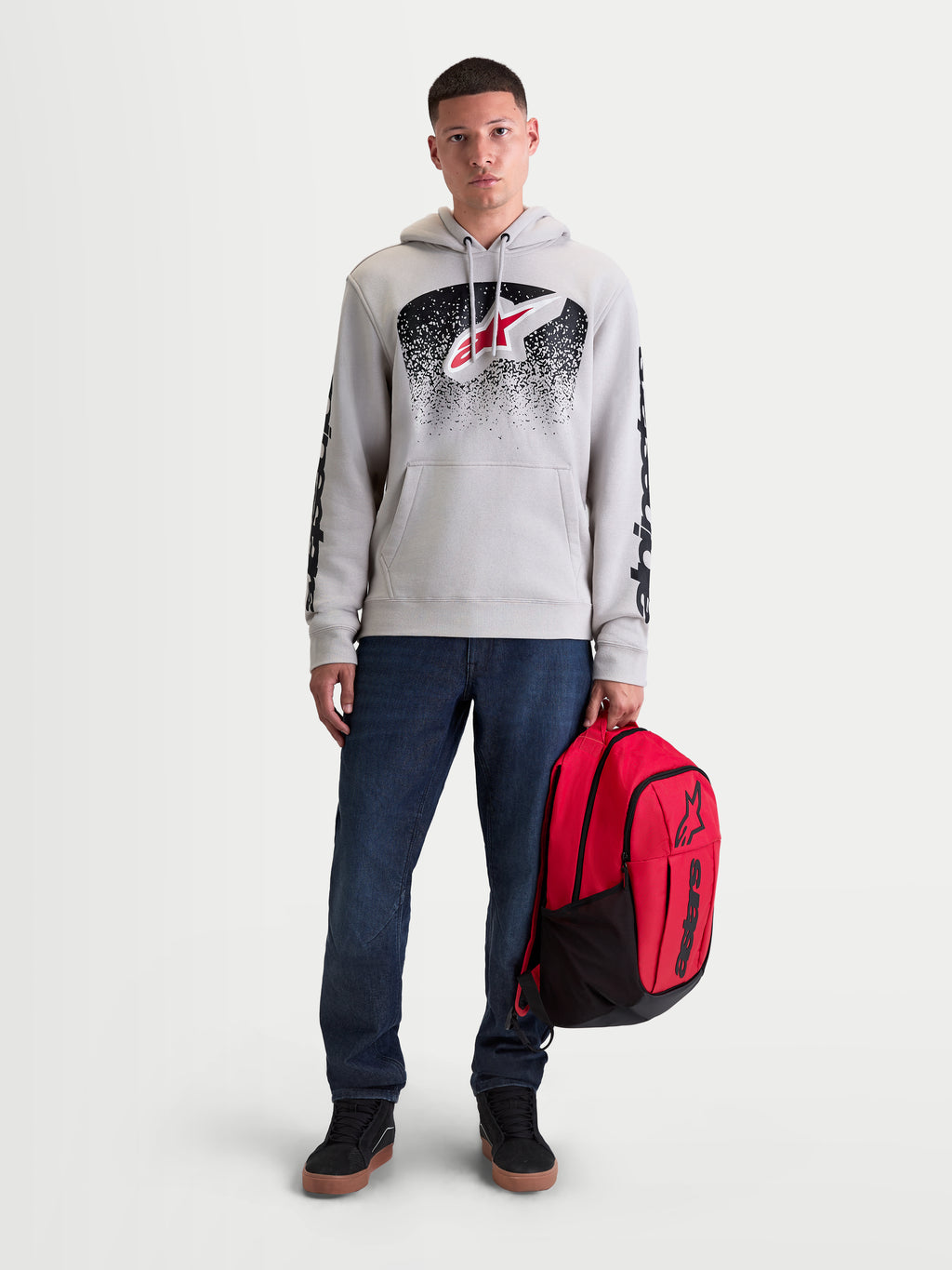 Alpinestars Zaino GFX Boss, zaino sportswear rosso e nero da 20 litri, poliestere 600D resistente con logo Astars in silicone a rilievo, tenuto da un modello per uso urbano casual.