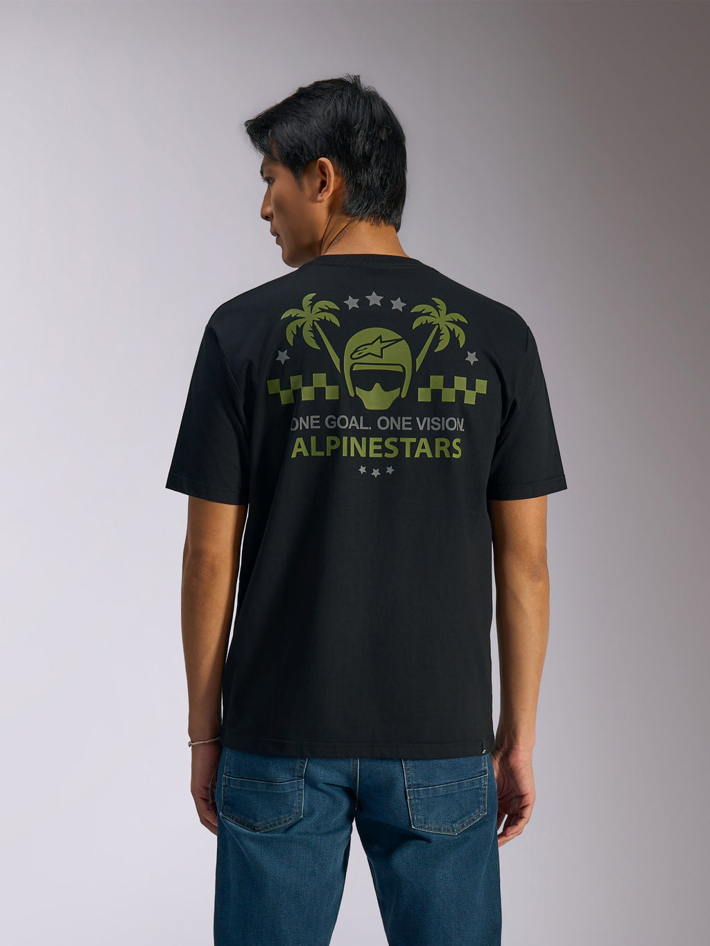Alpinestars Order CSF Tee, t-shirt a maniche corte, nero, vista posteriore, grafica verde oliva con palme e logo del casco, testo 'ONE GOAL. ONE VISION. ALPINESTARS', abbinata a jeans blu, streetwear casual motorsport