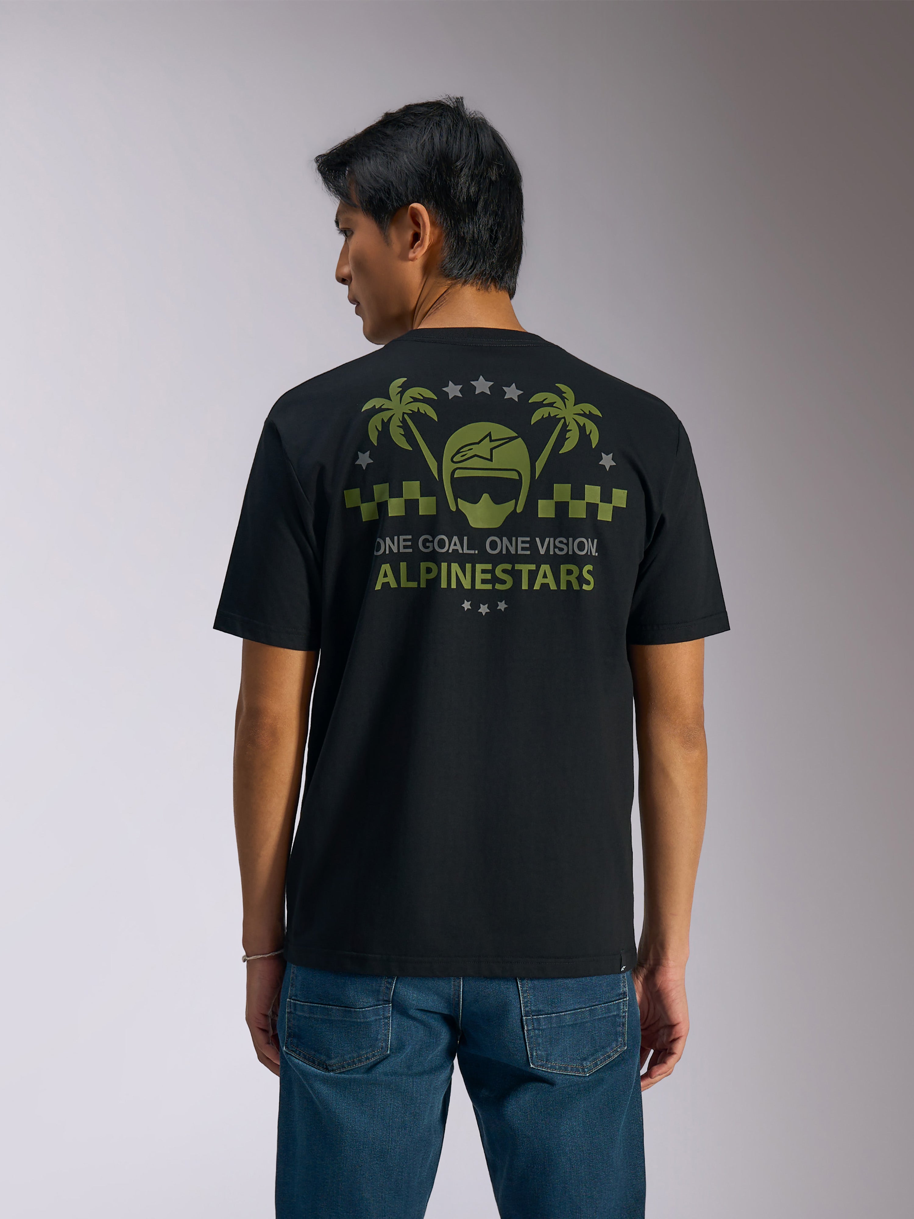 Alpinestars Order CSF Tee, t-shirt a maniche corte, nero, vista posteriore, grafica verde oliva con palme e logo del casco, testo 'ONE GOAL. ONE VISION. ALPINESTARS', abbinata a jeans blu, streetwear casual motorsport