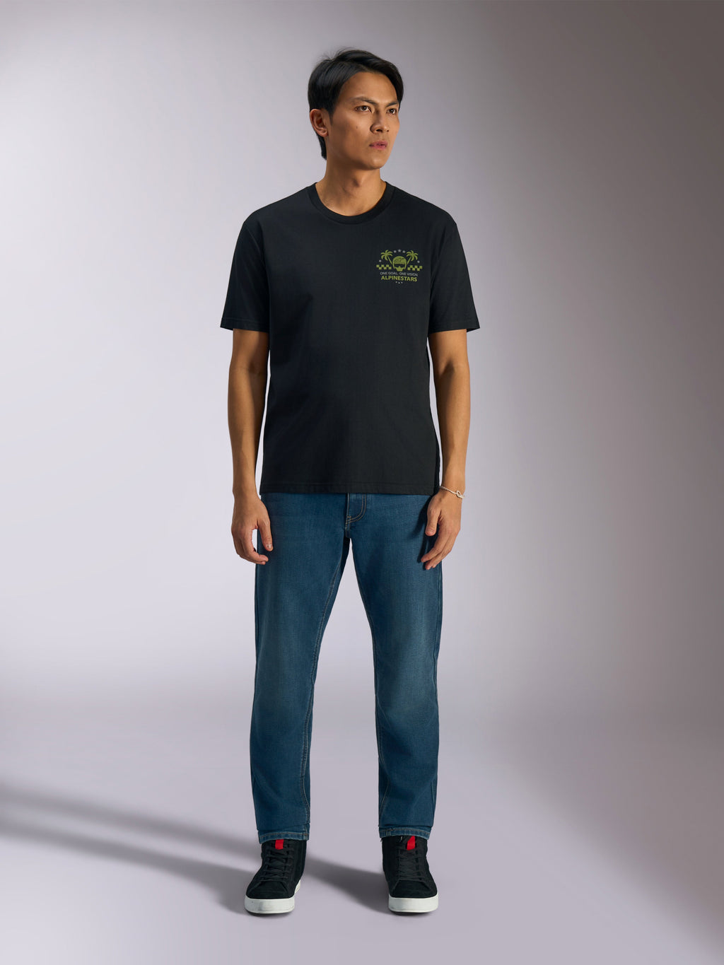 Alpinestars Order CSF Tee, maglietta a maniche corte, nera, grafica verde lime con casco e palme sul petto, indossata con jeans blu e sneakers nere, streetwear casual motorsport