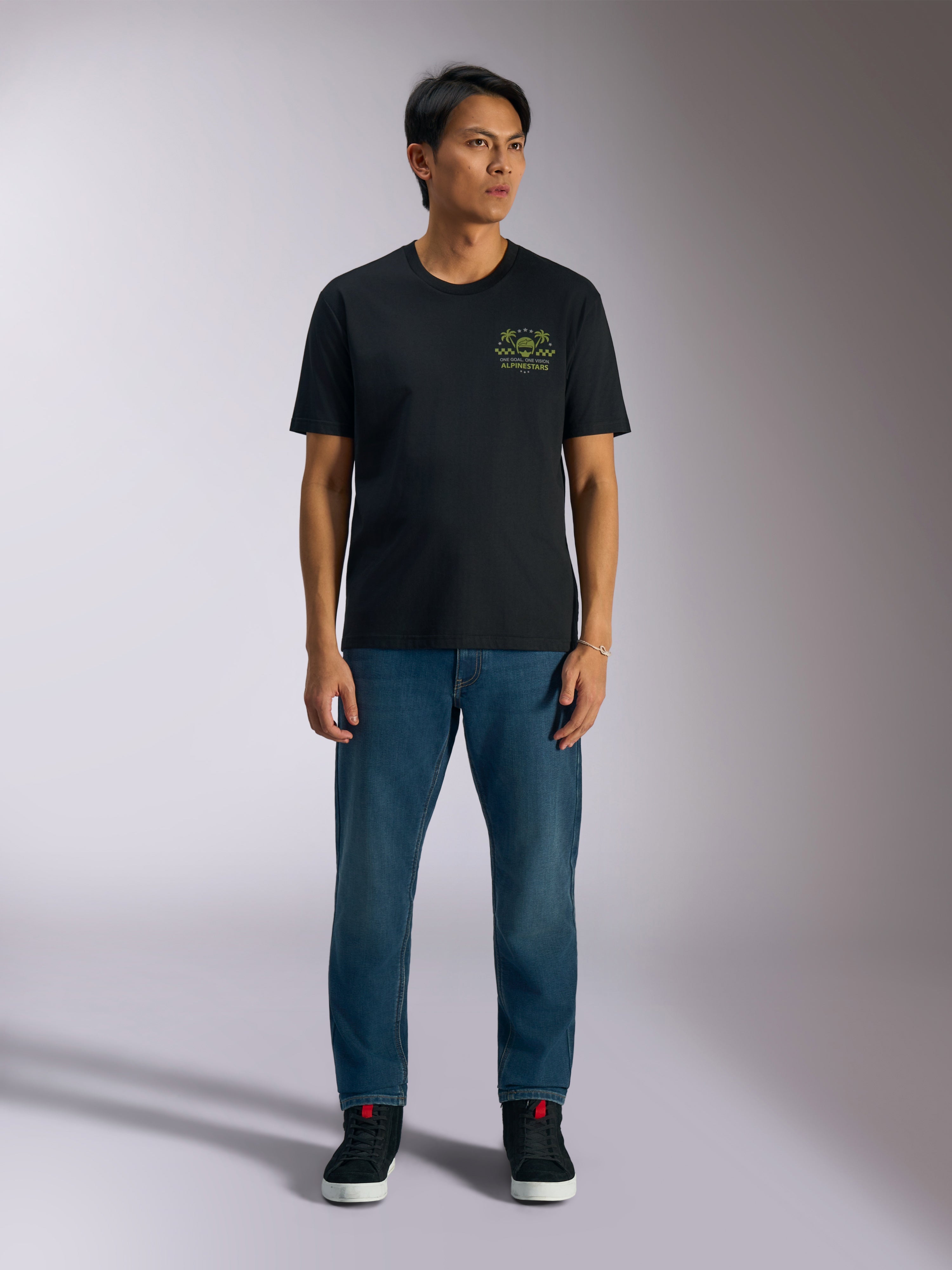 Alpinestars Order CSF Tee, maglietta a maniche corte, nera, grafica verde lime con casco e palme sul petto, indossata con jeans blu e sneakers nere, streetwear casual motorsport
